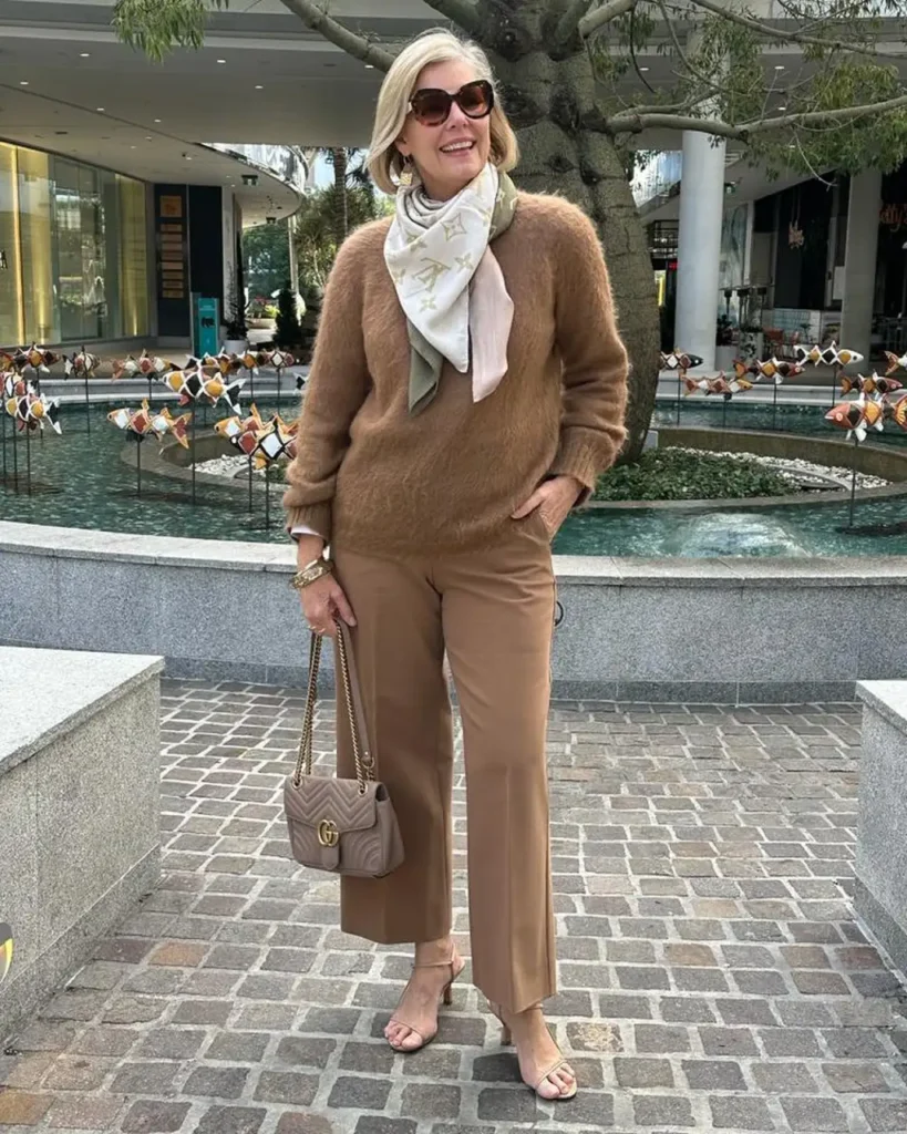 Stylish woman over 50 wearing a camel fuzzy sweater, matching cropped trousers, cream patterned scarf, and quilted handbag for an elegant casual winter outfit.