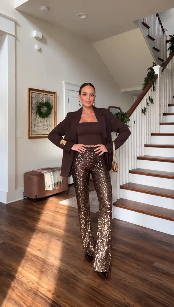 Woman wearing chocolate brown sequin wide-leg trousers with a matching brown blazer, fitted top, gold accessories, and pointed heels for a classy New Years Eve dinner outfit.