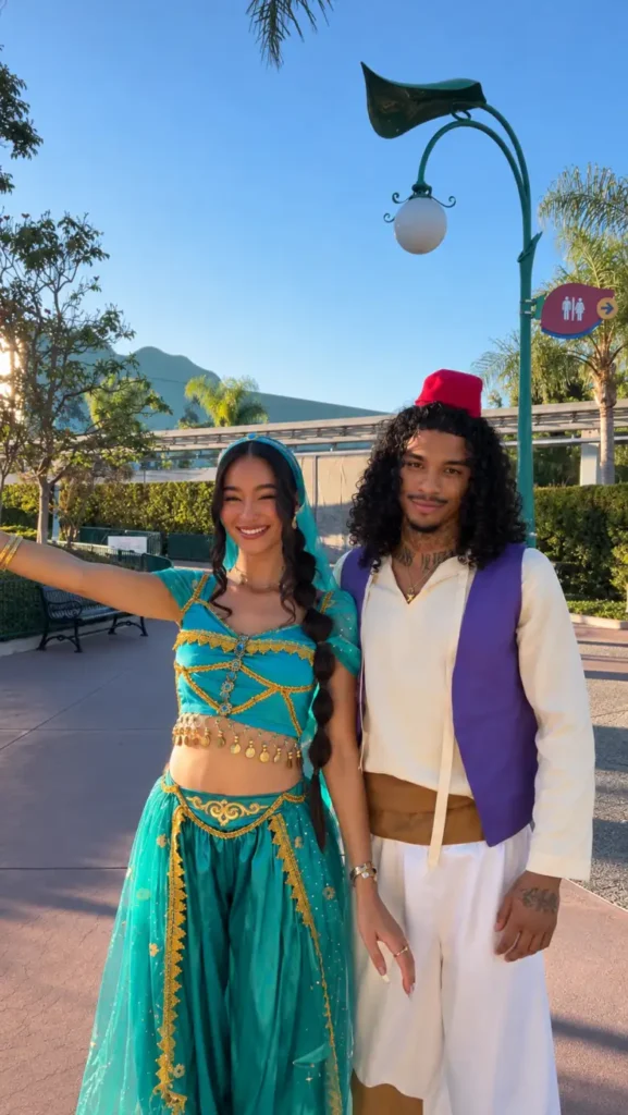 Couple dressed as Aladdin and Jasmine in turquoise, purple, white, and gold Halloween costumes.