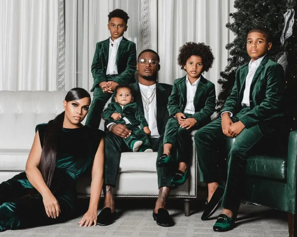 Family wearing coordinated emerald green velvet outfits, with Mom in a sleeveless dress, Dad in a green blazer, and four boys in matching velvet suits and white shirts.