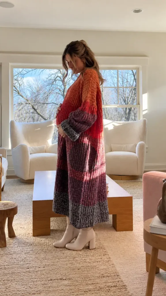 Pregnant woman wearing an oversized ombre knit sweater dress in burnt orange, burgundy, and charcoal with cream ankle boots for a cozy Thanksgiving outfit.