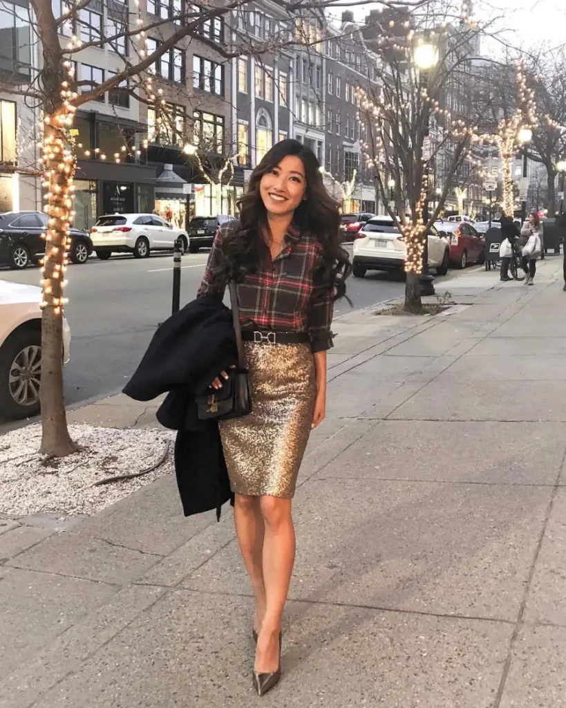 Petite woman wearing a plaid button-down shirt tucked into a gold sequin pencil skirt with pointed heels for a polished fall evening outfit.