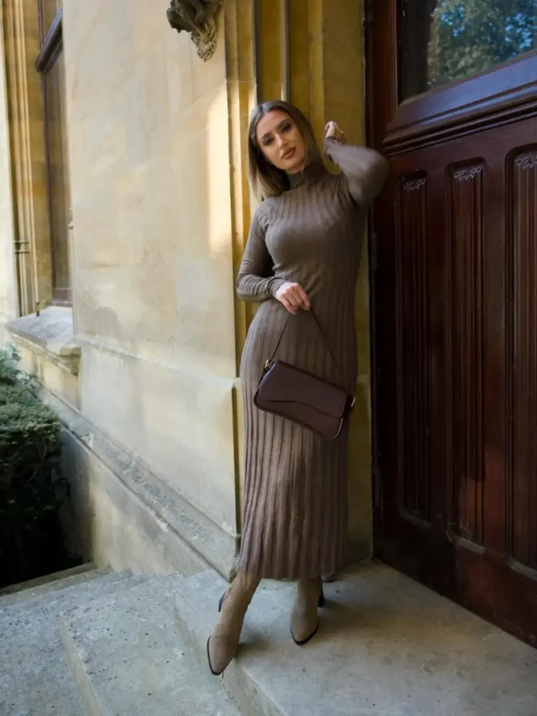 Woman wearing a taupe ribbed long-sleeve midi dress with neutral ankle boots and a dark brown shoulder bag for a polished fall look.