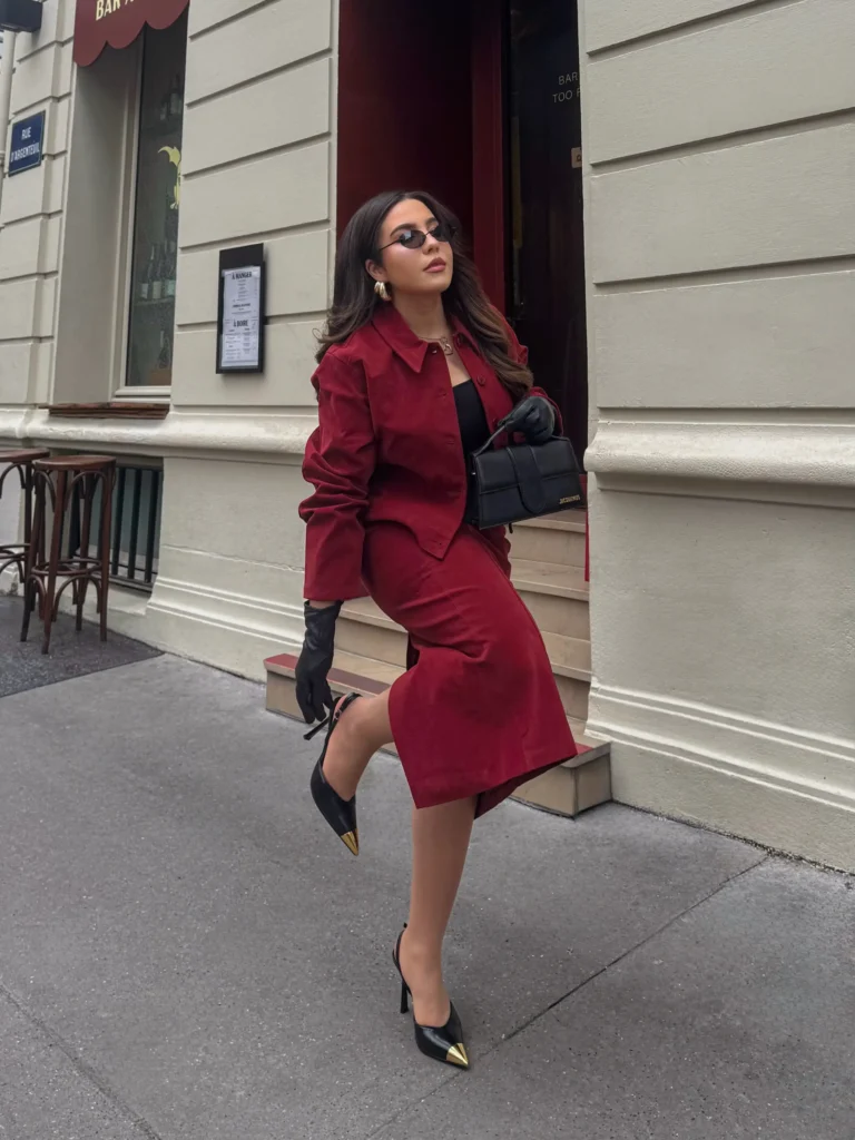 Burgundy matching jacket and midi skirt styled with a black top, pointed heels, gloves, and structured handbag for elegant fall fashion.