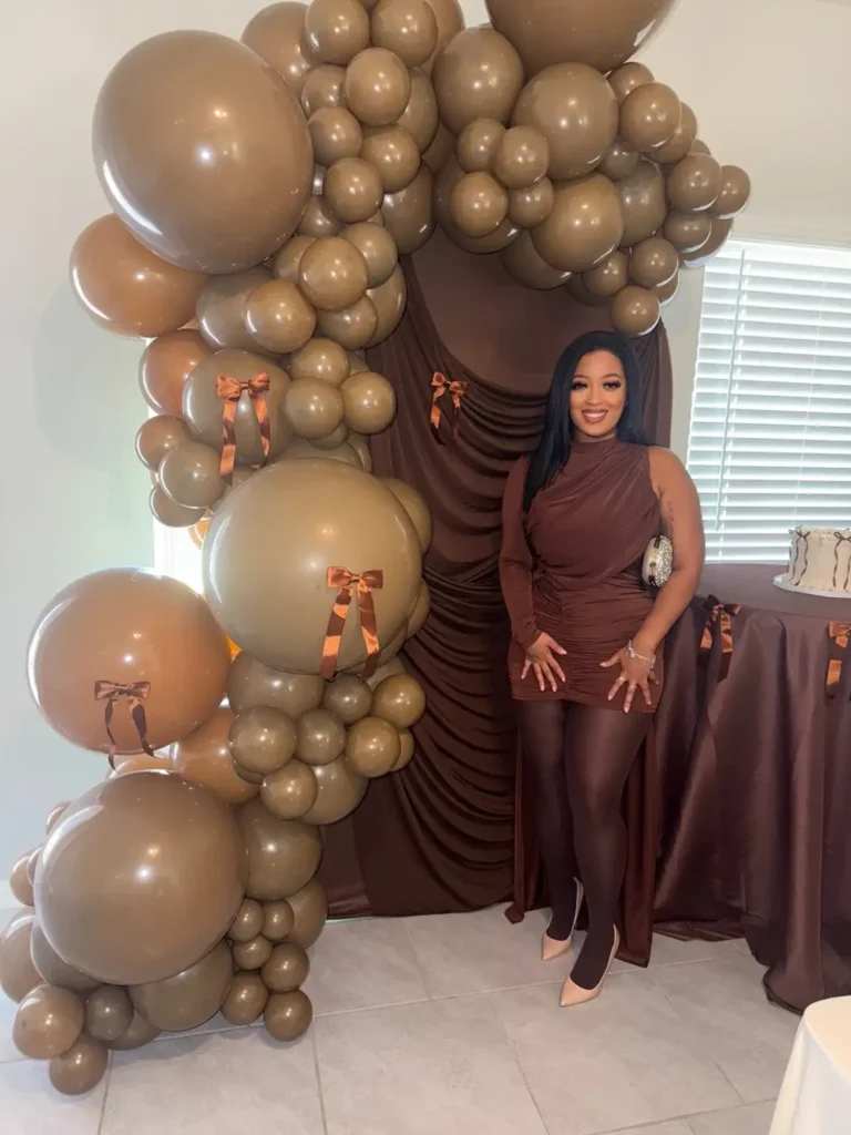 Woman wearing a chocolate brown asymmetrical ruched mini dress with matching brown tights, nude pointed heels, and sparkling clutch for a dressy Friendsgiving party.