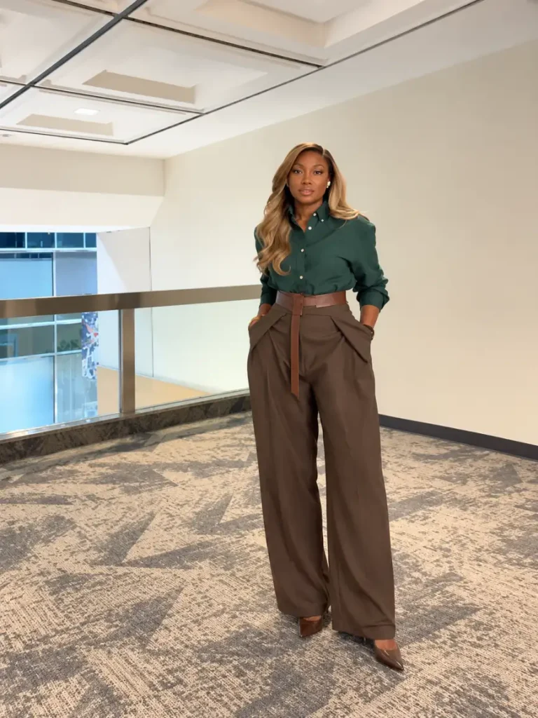 Black woman wearing a deep emerald green button-down blouse tucked into chocolate brown wide-leg trousers with a brown belt and pointed heels for fall office wear.