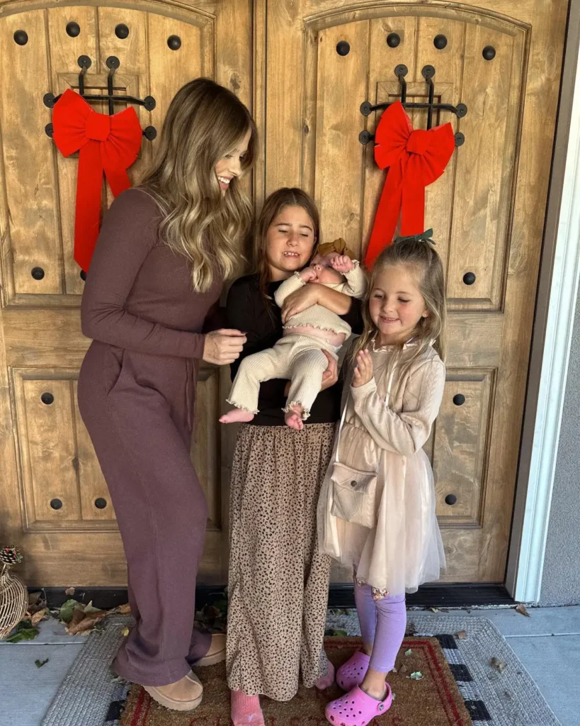 Mom wearing a mauve knit outfit with three children in a leopard-print maxi skirt, cream ribbed baby clothes, and a beige tulle dress with lilac leggings and pink clogs.