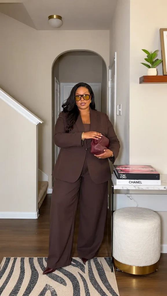 Curvy Black woman wearing a chocolate brown tailored blazer with matching wide-leg trousers, burgundy pointed heels, and a wine-colored clutch for an elegant fall work outfit.