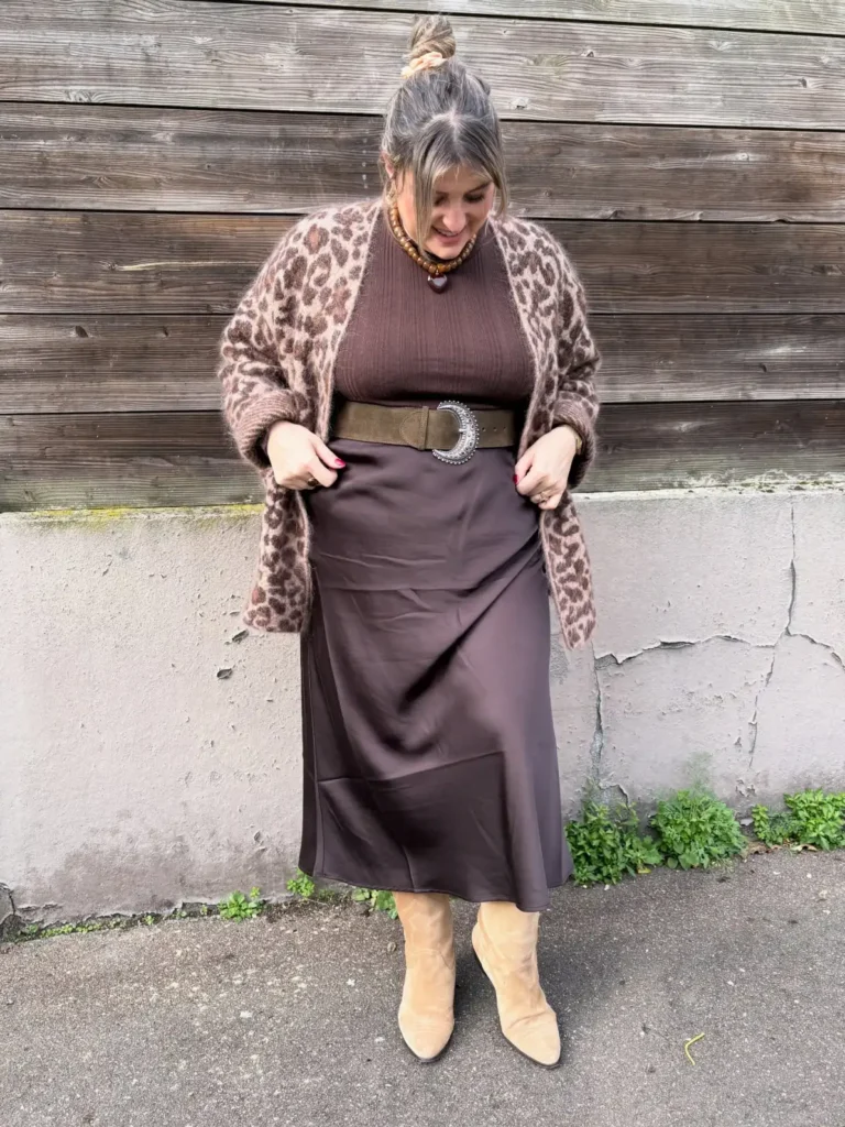 Plus size woman wearing a chocolate brown top and midi skirt with a leopard print cardigan, statement belt, and tan boots for fall.