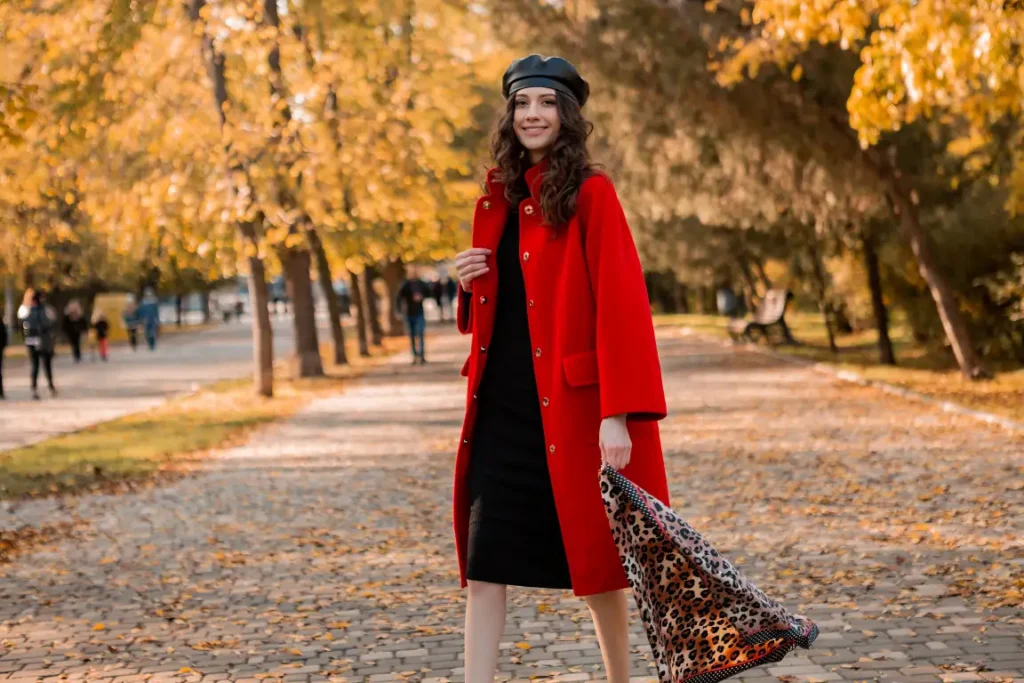 Woman wearing a bright red long coat over a black dress with a black beret and leopard-print scarf for a stylish autumn Thanksgiving outfit.
