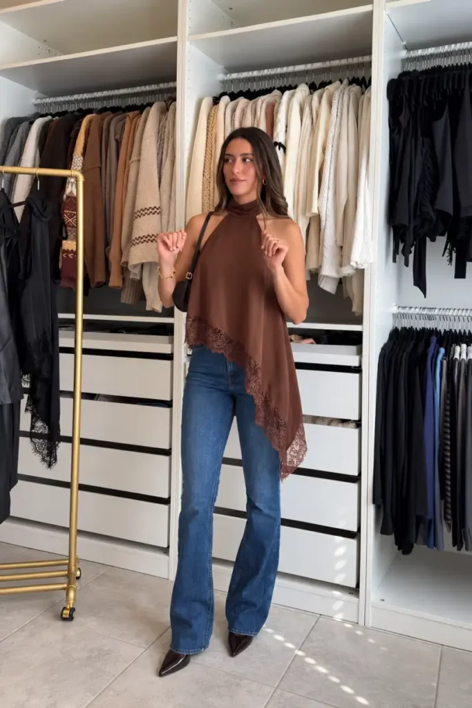 Woman wearing a chocolate brown halter top with an asymmetrical lace-trimmed hem, blue bootcut jeans, and dark pointed-toe heels for a dressy Thanksgiving dinner outfit.