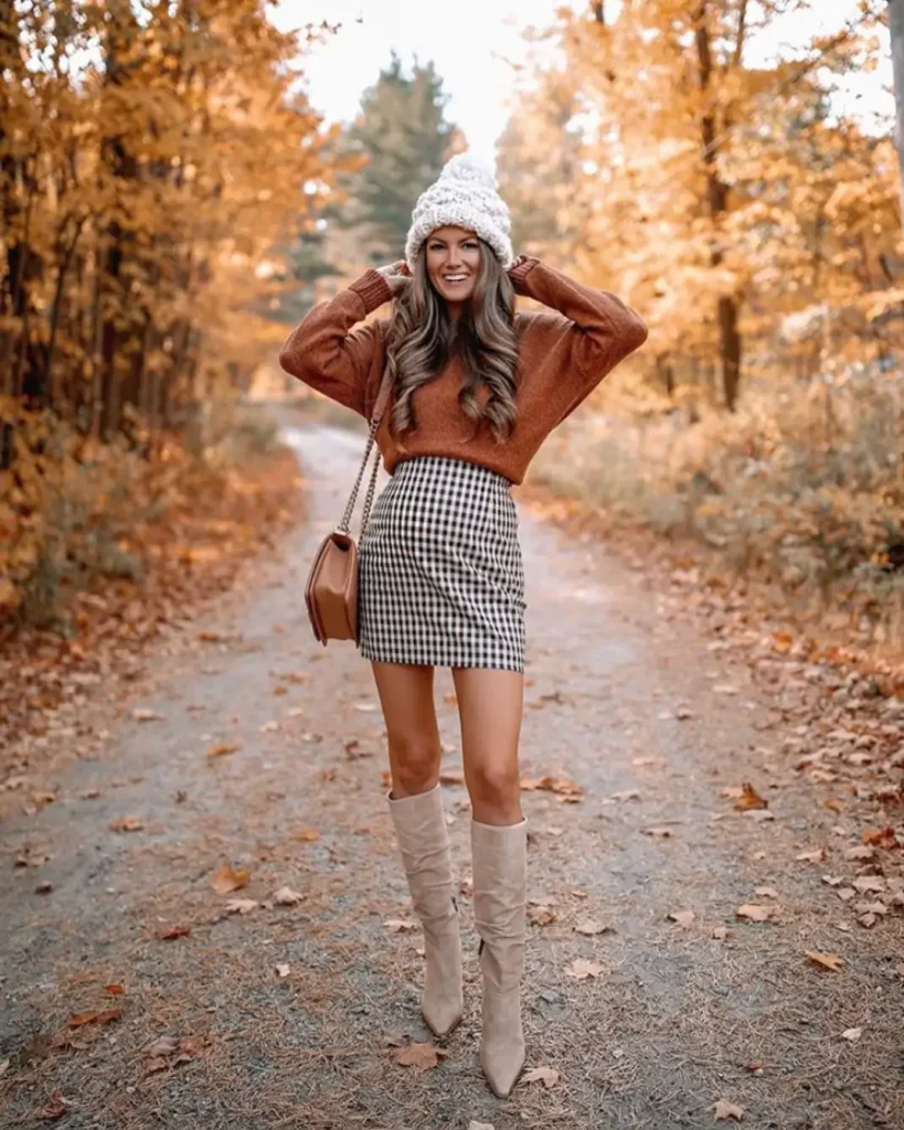 Rust sweater paired with checked mini skirt, cream knit beanie, tan handbag, and beige knee-high boots.