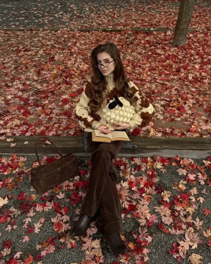 Woman wearing a cream and brown chunky patterned sweater with chocolate flared trousers, brown ankle boots, and a suede bag for a cozy fall outfit.
