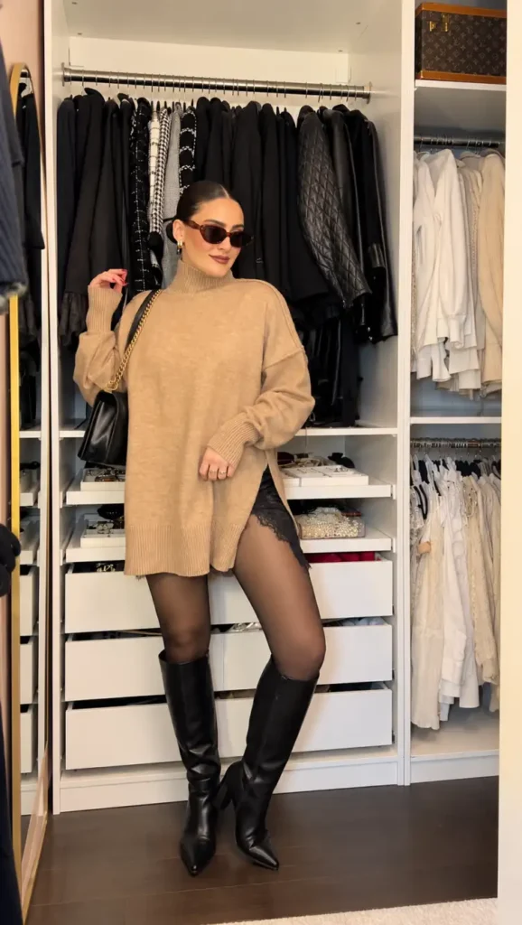 Woman wearing an oversized camel turtleneck sweater over black lace-trim mini bottoms, sheer black tights, knee-high leather boots, and a black shoulder bag for a cozy dressy winter outfit.