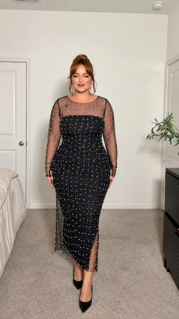 Plus-size woman wearing a fitted black midi dress with crystal-embellished sheer mesh sleeves, a leg slit, and black pointed heels for a glamorous evening party look.