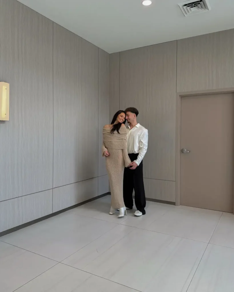 Couple wearing elegant Thanksgiving outfits with a champagne off-the-shoulder knit maxi dress, white ankle boots, glossy ivory shirt, relaxed black trousers, and white sneakers.