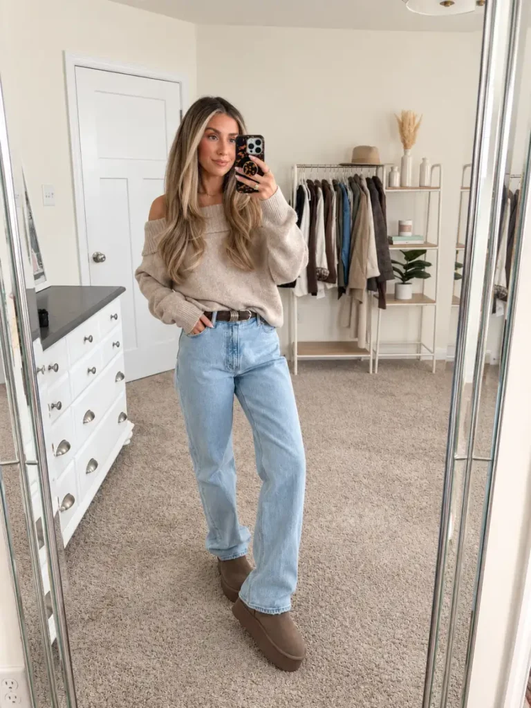 Woman wearing a beige off-shoulder knit sweater with light-wash straight-leg jeans, a dark brown belt, and taupe platform ankle boots for a casual Thanksgiving outfit.