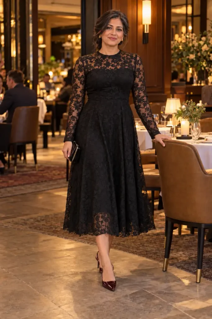 Mature woman wearing a black floral lace midi dress with sheer long sleeves, a high neckline, flared skirt, and oxblood slingback heels for a classy New Years Eve dinner look.