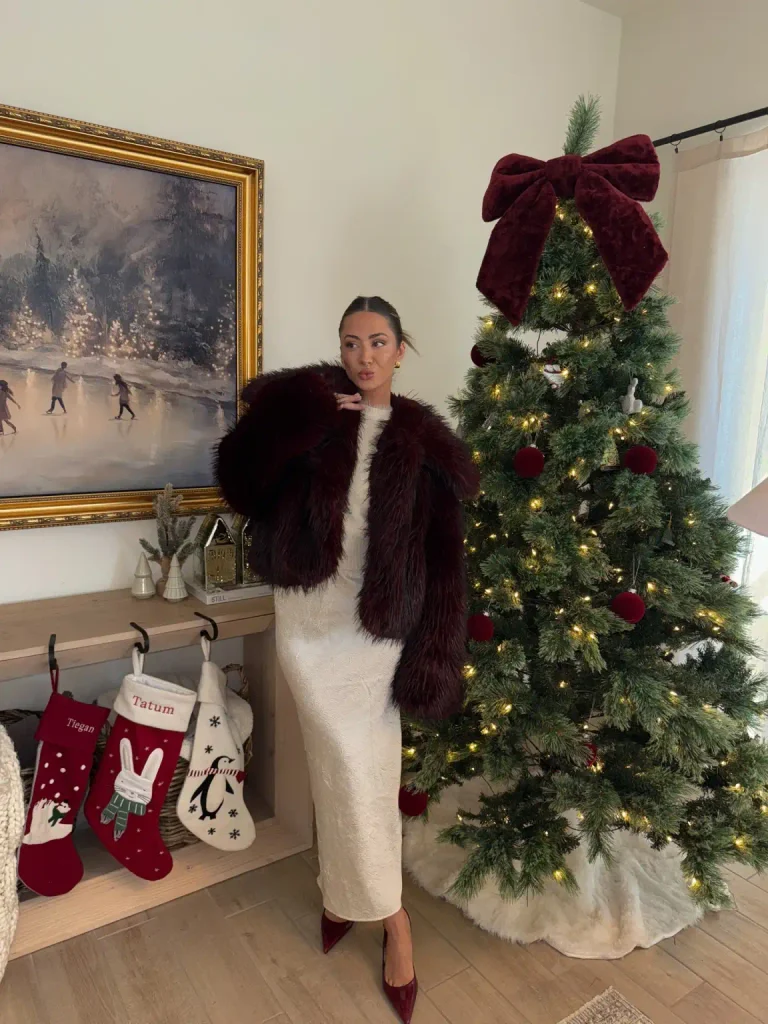 Woman wearing a cream fitted midi dress with a burgundy faux fur jacket and matching burgundy pointed heels for a glamorous Christmas dinner outfit.