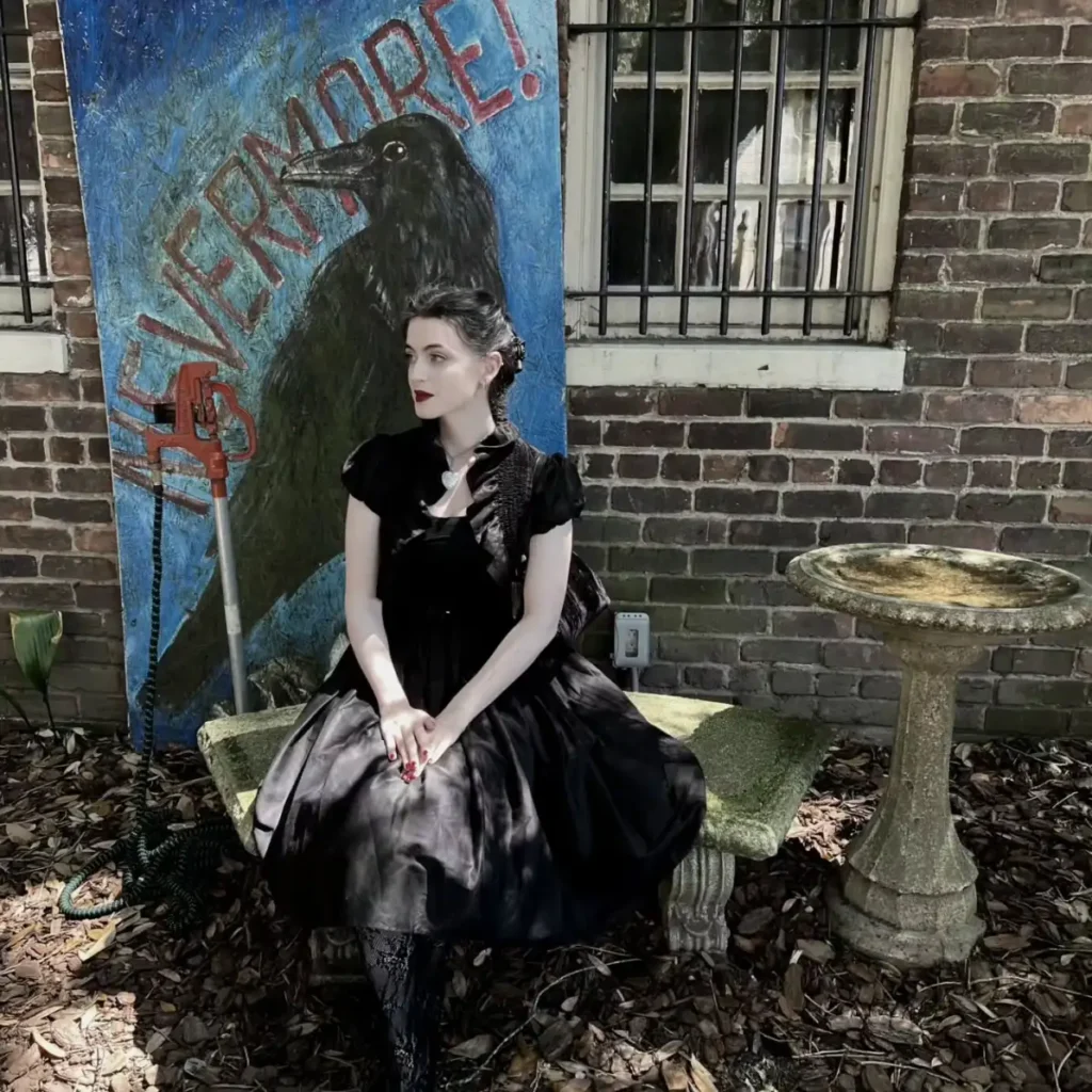 Woman wearing a full black gothic dress with puff sleeves, dark lipstick, vintage necklace, and pinned-up hair for a raven-inspired Halloween look.