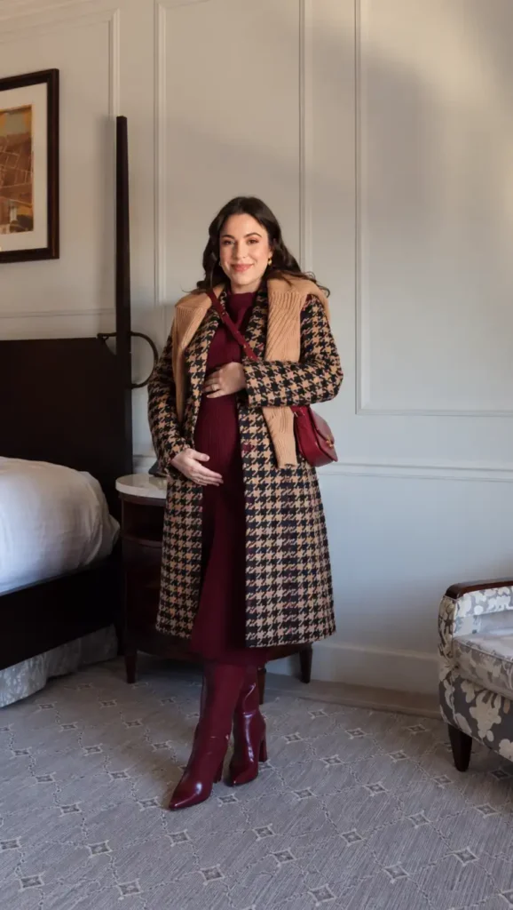 Pregnant woman styling a burgundy knit midi dress with a brown and black houndstooth coat, burgundy knee-high boots, and a matching crossbody bag for Thanksgiving.