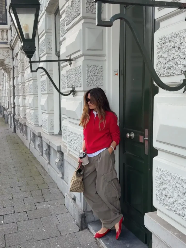 Woman wearing a bright red knit sweater with relaxed taupe cargo pants, red pointed flats, and a patterned handbag for a colorful casual fall outfit.