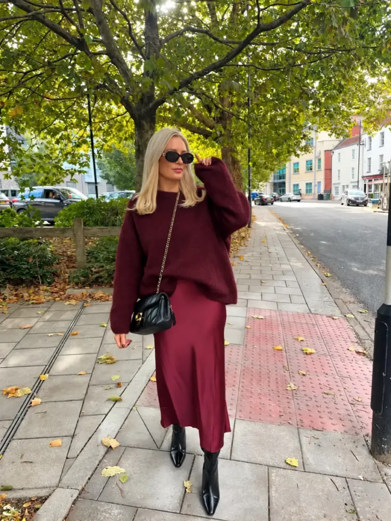 Oversized burgundy sweater with a matching burgundy satin midi skirt, black ankle boots, and black crossbody bag.