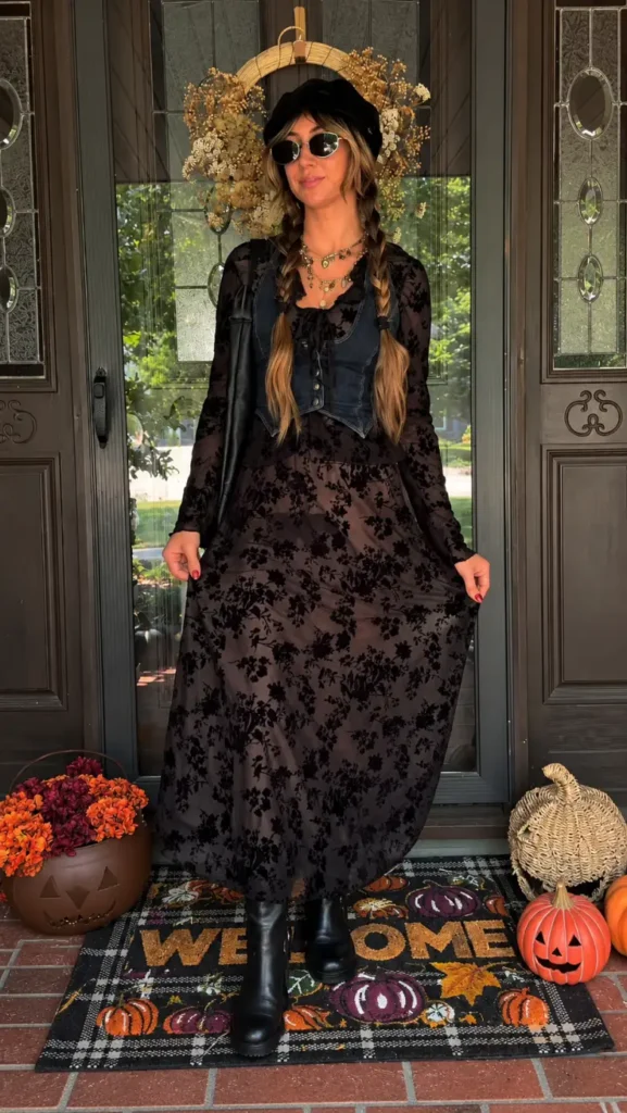 Woman wearing a sheer black floral maxi dress with denim vest, black cap, round sunglasses, layered necklaces, braids, and ankle boots.