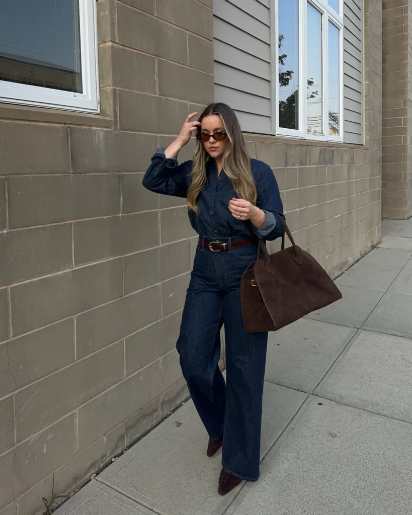 Woman wearing a dark indigo denim button-down shirt with matching wide-leg jeans, a brown belt, pointed brown boots, and a large suede-style tote.