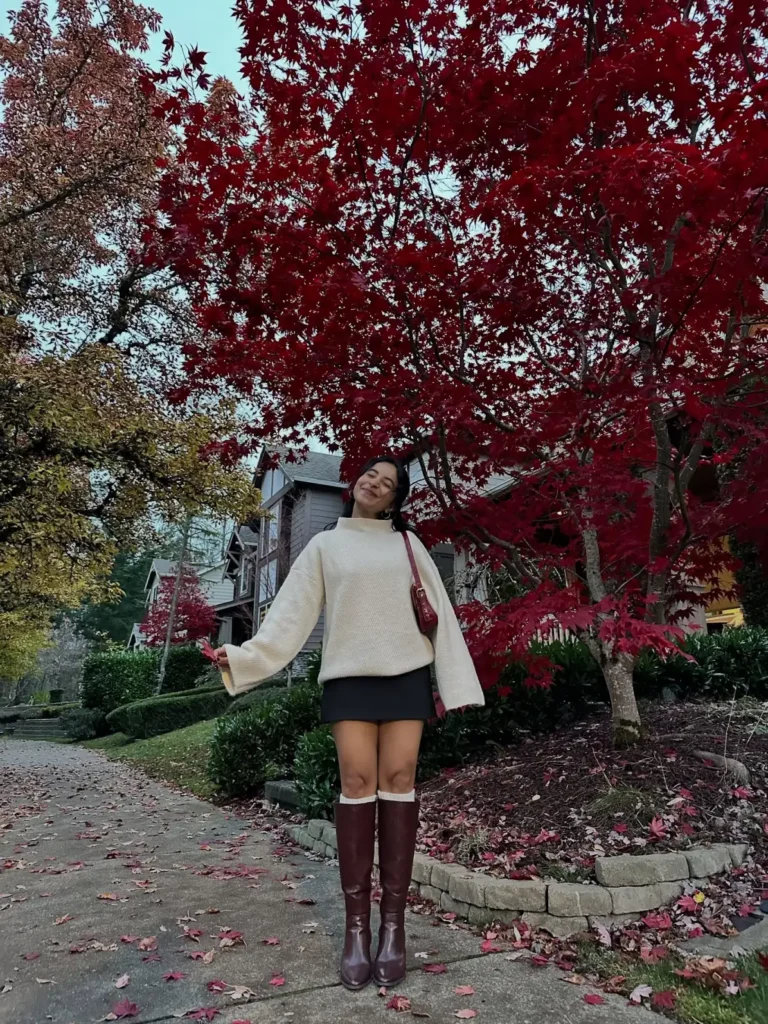 Oversized cream sweater paired with black mini skirt, brown knee-high boots, white socks, and burgundy shoulder bag.