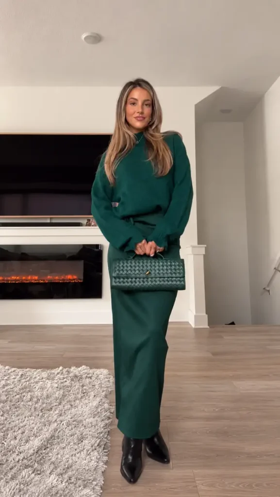Woman wearing an emerald-green oversized sweater with a matching green maxi skirt, black pointed boots, and a woven green handbag for a classy winter holiday outfit.