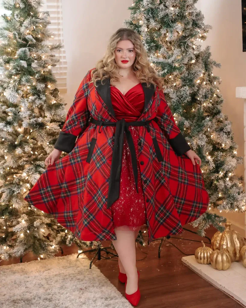 Plus-size woman wearing a red tartan belted coat with black lapels over a red sparkly dress, finished with matching red pointed heels for a festive Christmas outfit.