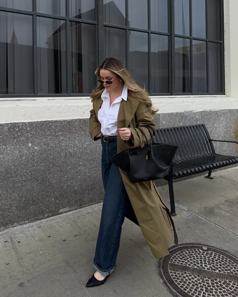 Woman wearing an olive trench coat over a crisp white shirt with dark wide-leg jeans, black pointed flats, and a large black tote for a polished fall outfit.