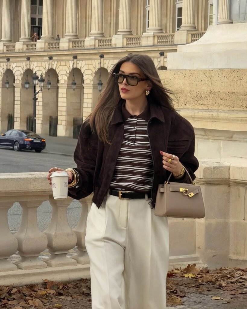 Dark brown jacket layered over a brown and white striped top with cream wide-leg trousers and a taupe handbag for polished fall fashion.