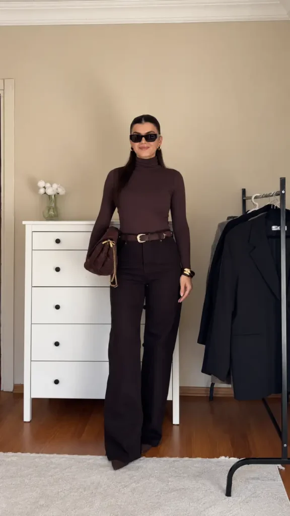 Woman wearing a fitted chocolate brown turtleneck with matching high-waisted wide-leg pants, a brown belt, pointed heels, and a matching handbag for a classy Thanksgiving dinner look.