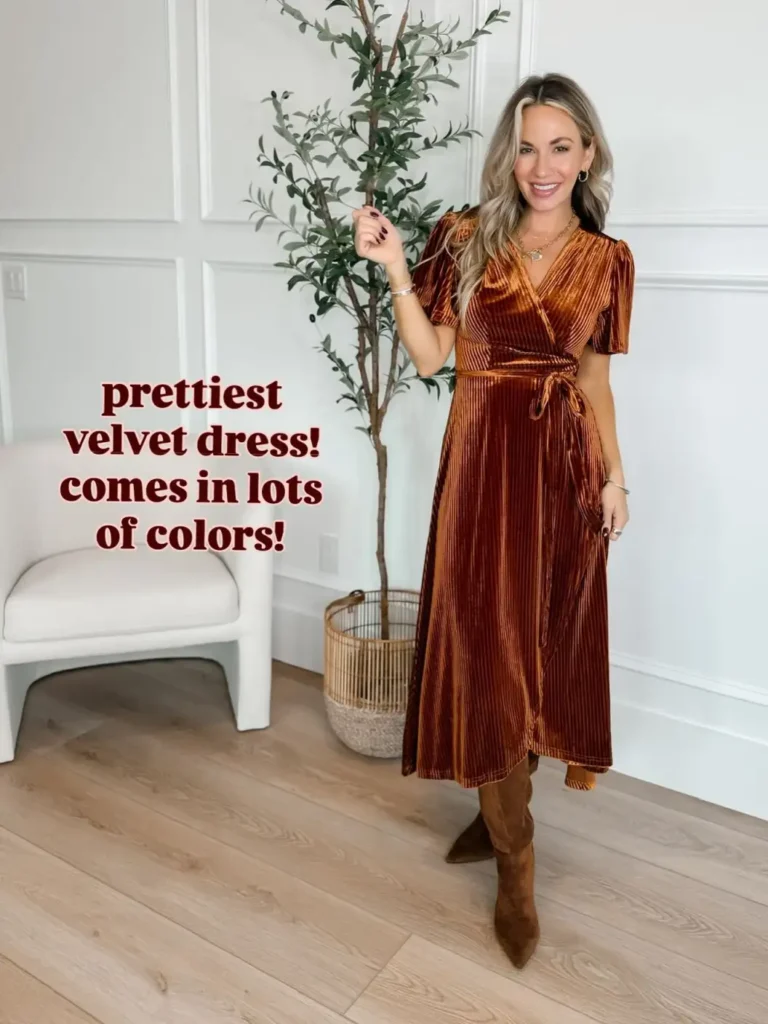 Woman wearing a copper brown velvet wrap midi dress with short sleeves, a tie waist, layered gold necklaces, and tall brown boots for an elegant Friendsgiving outfit.