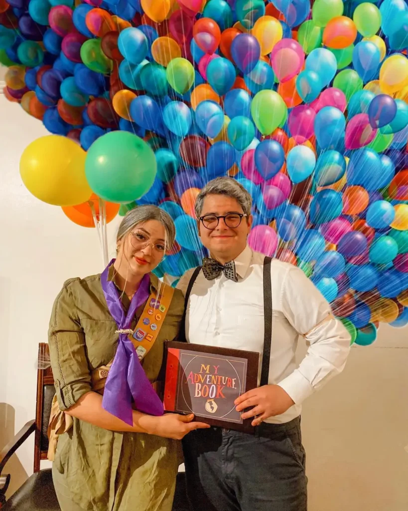 Carl and Ellie inspired couple costume from Up with glasses, suspenders, badges, Adventure Book, and balloons.