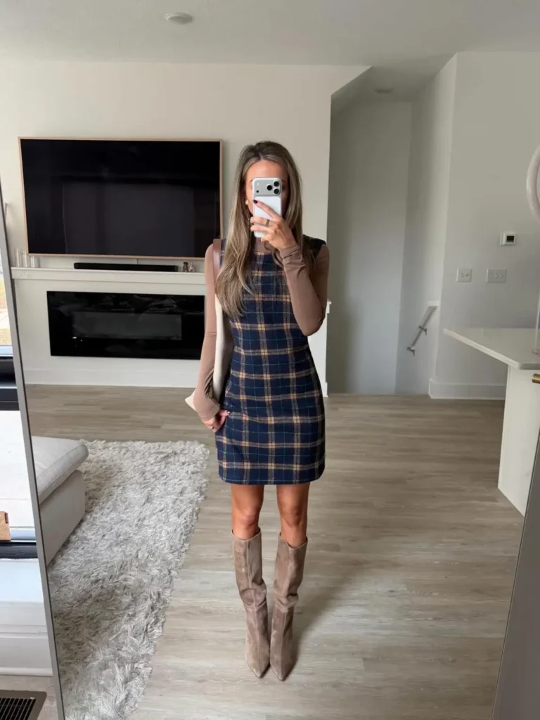 Woman wearing a navy and tan plaid mini dress over a taupe long-sleeve top with tall taupe suede boots and a light shoulder bag for a preppy fall outfit.