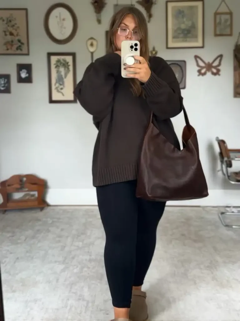 Plus size woman wearing an oversized chocolate brown sweater with black leggings, neutral ankle boots, and a large brown shoulder bag for fall.