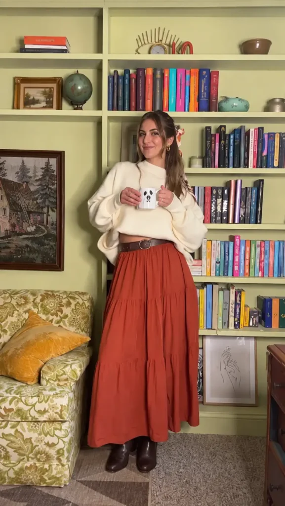Cream oversized sweater tucked into a rust tiered maxi skirt with a brown waist belt and brown ankle boots.