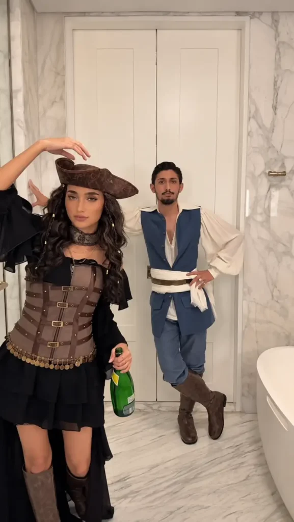 Couple wearing coordinated pirate costumes with a corset, pirate hat, billowy shirt, boots, belts, and sash.