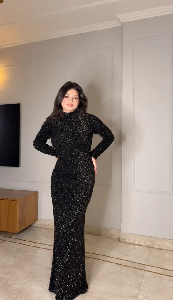 Woman wearing a fitted floor-length black sequin gown with long sleeves and a high neckline for an elegant formal New Year's Eve party outfit.