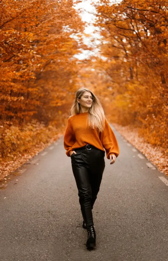 Woman wearing an oversized burnt orange sweater with black leather-look trousers, a black belt, and chunky lace-up boots for a cozy Thanksgiving fall outfit.