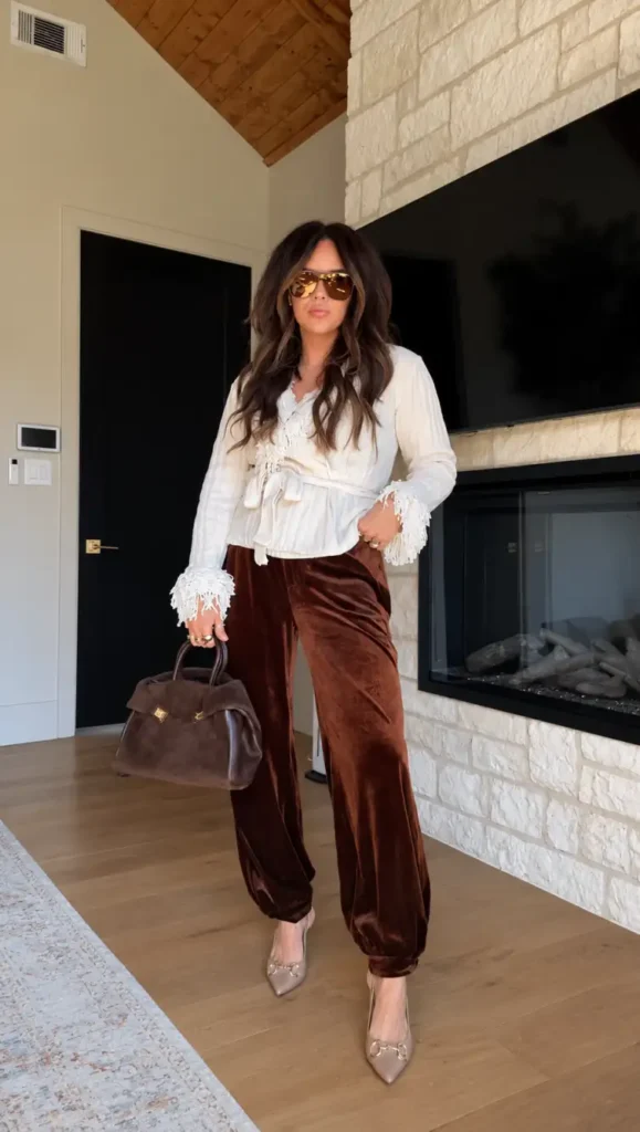 Woman wearing chocolate brown velvet wide-leg trousers with an ivory lace-trimmed blouse, pointed nude heels, and a brown handbag for an elegant fall dinner outfit.