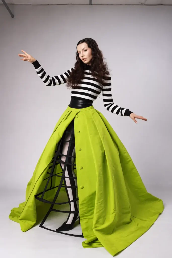 Woman wearing a black and white striped top with a dramatic neon green floor-length skirt and black cage detail for a bold Halloween costume.