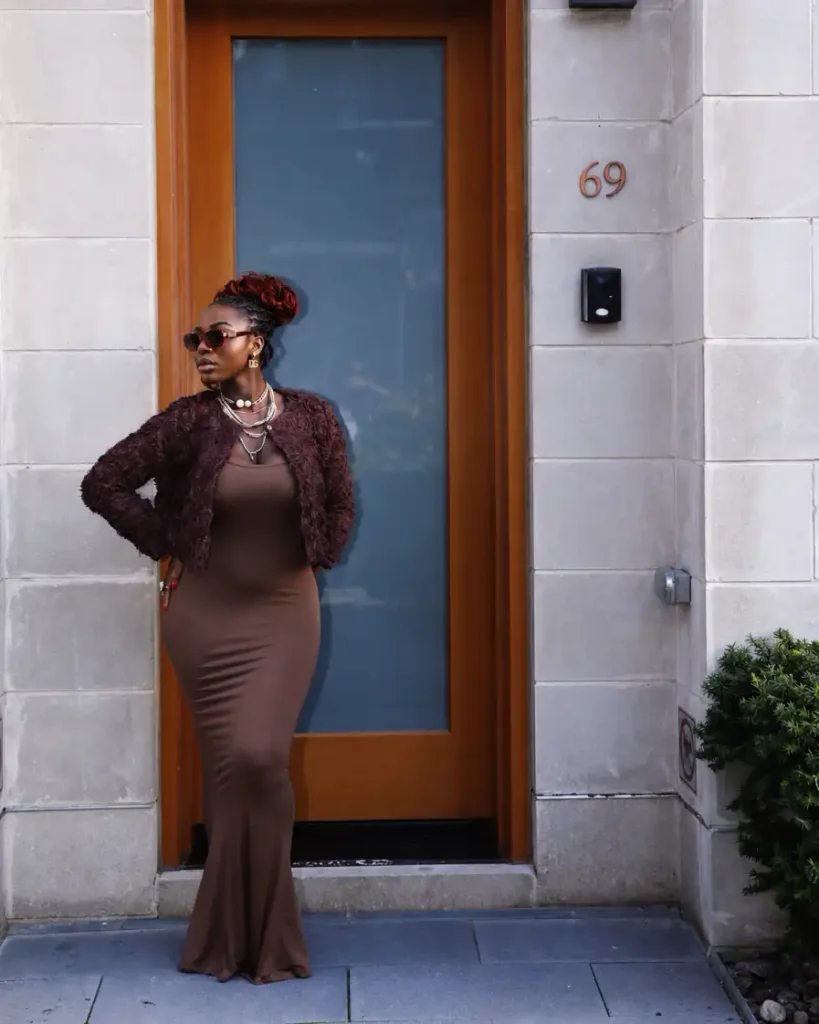 Curvy Black woman wearing a fitted chocolate brown maxi dress with a textured cropped jacket, layered necklaces, and sunglasses for a trendy autumn fashion look.