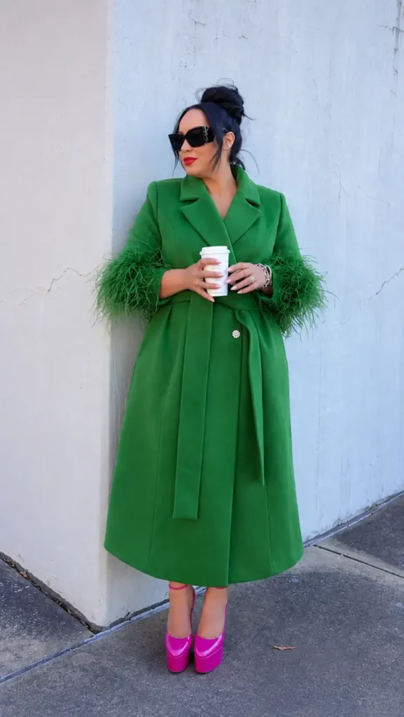 Plus size Black woman wearing a belted emerald green statement coat with textured cuffs and bright pink platform heels for a bold fall look.