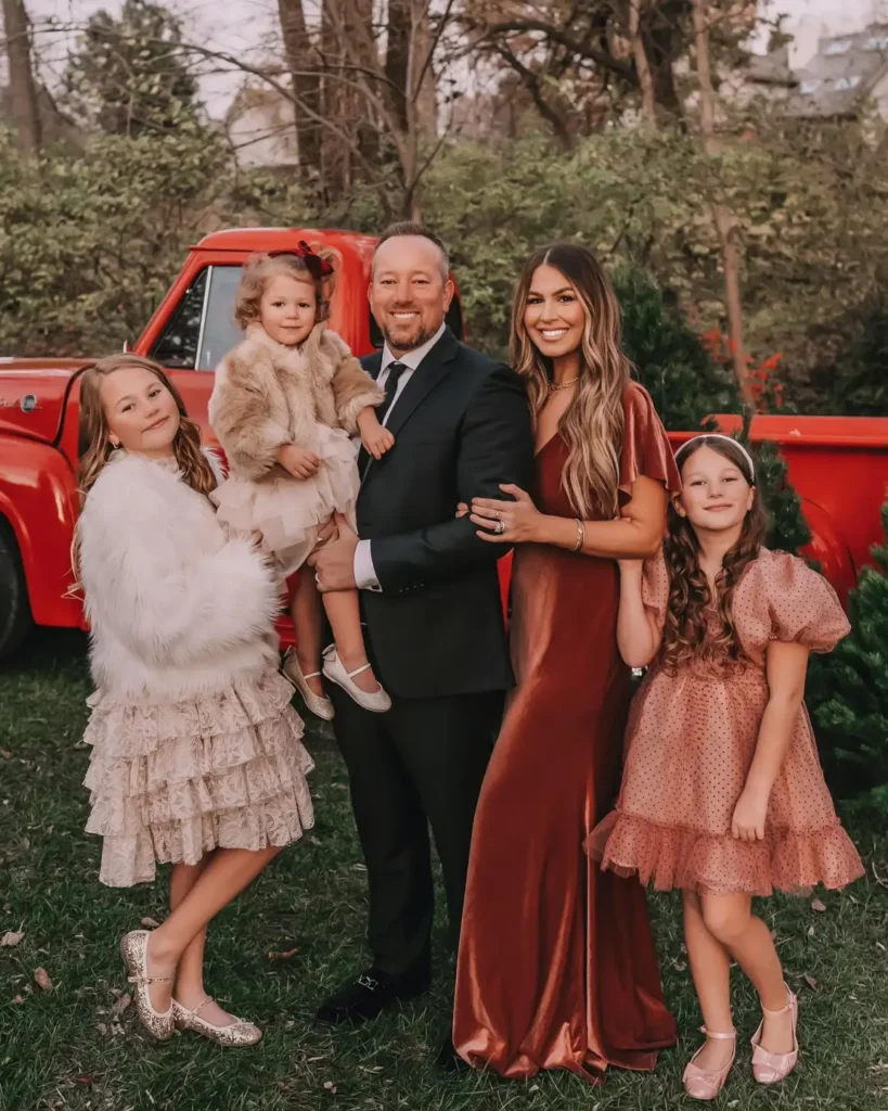 Family wearing elegant Thanksgiving outfits with Mom in a rust maxi dress, Dad in a black suit, and three daughters in cream and blush dresses with fluffy layers and sparkly shoes.