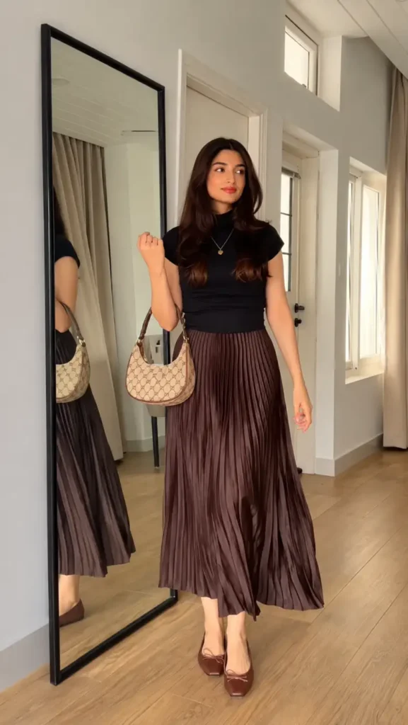 Black fitted top paired with a chocolate brown pleated maxi skirt, brown flats, and a patterned shoulder bag.