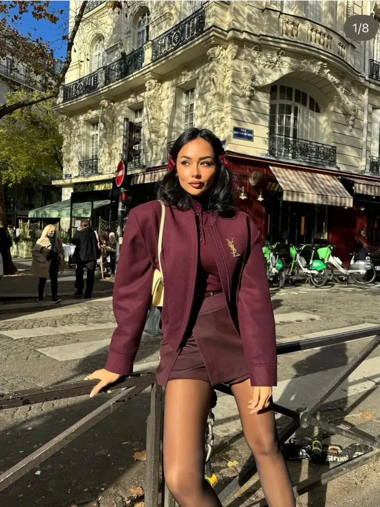Woman wearing a structured burgundy jacket with matching shorts and high-neck top, paired with a small cream shoulder bag for a polished Paris-inspired fall look.